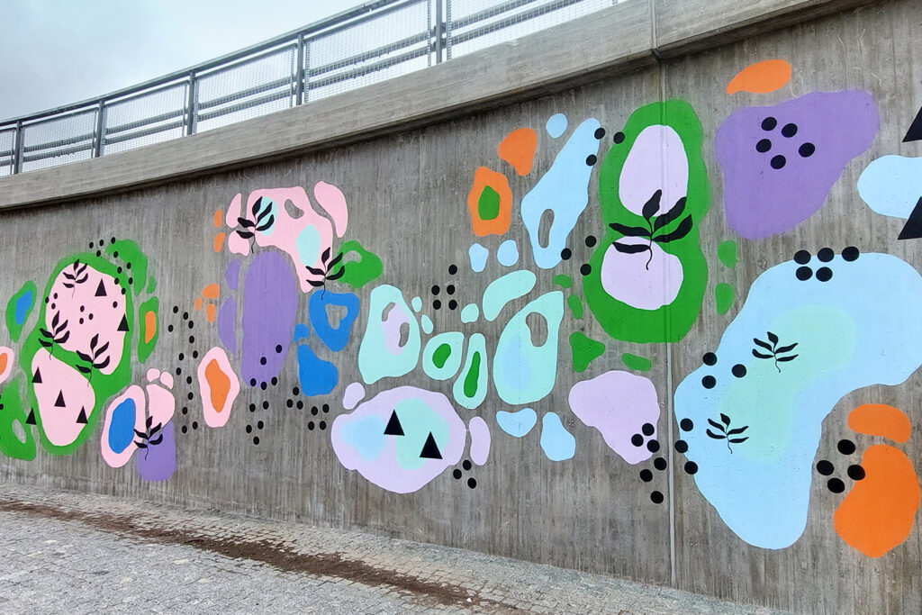 Sillan kupeessa oleva muraali, joka koostuu abstrakteista värikkäistä pinnoista sekä mustista graafisista muodoista.