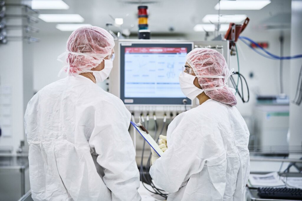Kaksi suojavaatteisiin pukeutunutta henkilöä työskentelee laboratoriossa.