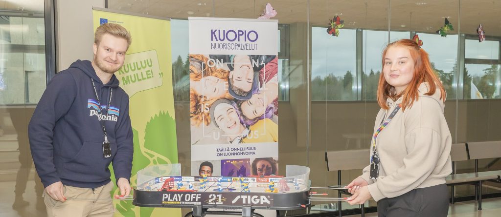 Kaksi henkilöä pelaamassa pöytäkiekkoa oppilaitoksen aulassa.