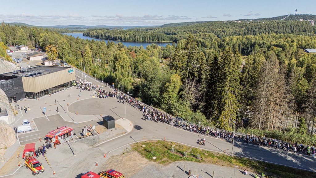 Ihmisjoukko vaeltaa Luolaan. Ympärillä metsä ja järvi.